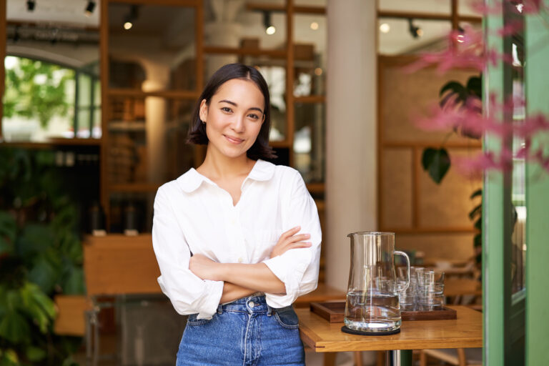 Portrait of smiling asian girl in white collar shirt, working in cafe, managing restaurant, looking confident and stylish